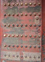 An old door with rivets and a lot of the red paint worn off.