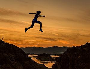Person jumping over a gully at sunset